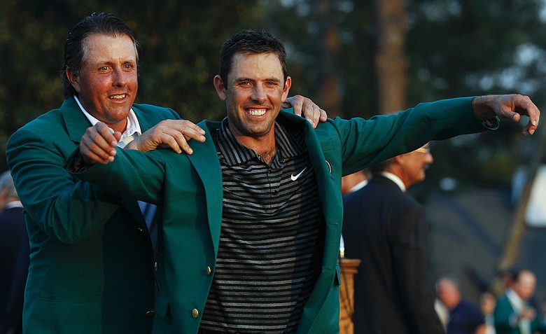Former champion Phil Mickelson, back, helps Charl Schwartzel of South Africa with his green Masters jacket after winning the Masters golf tournament Sunday, April 10, 2011, in Augusta, Ga.