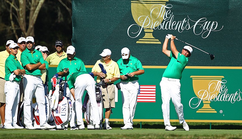 Phil Mickelson tees off during Presidents Cup practice as his teammates look on.
