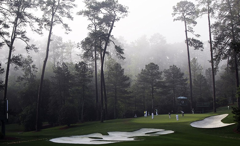 Players putt on the 10th green in the morning fog during a practice round for the Masters.