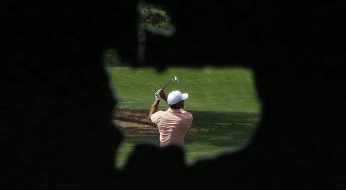 In a photo taken through a metal cutout of the Masters' logo, Tiger Woods hits on the driving range during a practice round for the Masters.