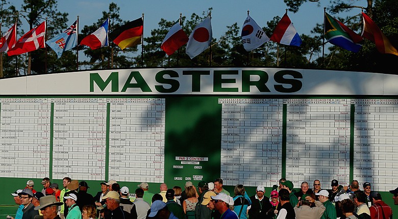Patrons walk in front of a leaderboard near the first fairway during a practice round prior to the start of the 2014 Masters.