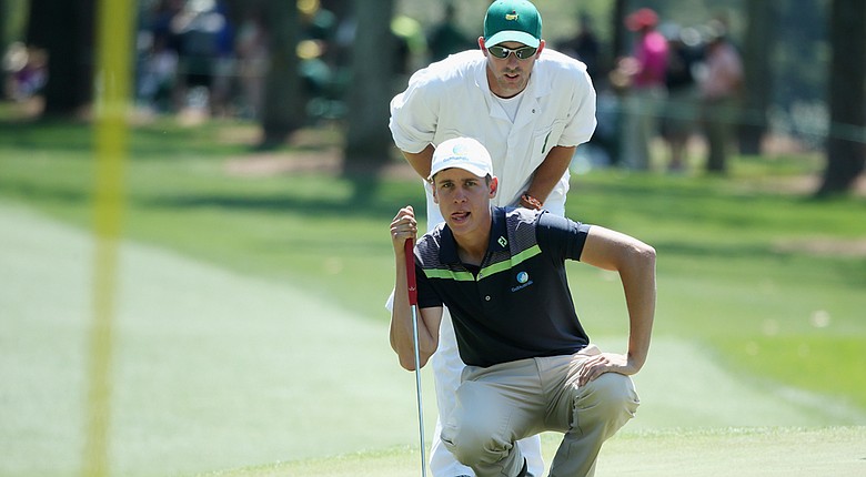 Oliver Goss lines up a putt on the first green with the help of caddie Brian Tam at the 2014 Masters.