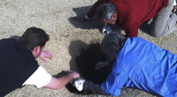 In this cell phone image taken March 8, 2013, Hank Martinez, top, Ed Magaletta, right, and Russ Nobbe, look into an 18-foot-deep sinkhole that golfer Mark Minhal fell into at Annbriar Golf Course in Waterloo, Ill. (Courtesy of golfmanna.com, Mike Peters)