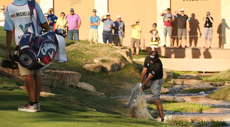 Phil Mickelson hits a shot from the edge of a water hazard at the par-5 18th during the second round of the Valero Texas Open. Mickelson birdied the hole.